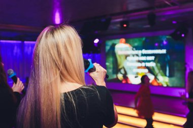 Mutlu sarışın şarkı karaoke barda mikrofon içine.