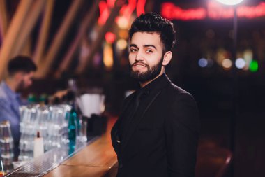 Bar tezgahında kokteyl içen yakışıklı genç adam, iş kıyafeti giyiyor.