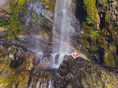 Genç bir adam Yoga dağlarda bir şelale ile nişanlandı. Gökkuşağı