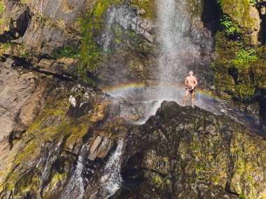 Havada silah ile şelaleler tarafından ayakta çekici adam. Gökkuşağı
