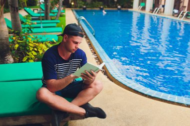 Bahçede yüzme havuzunun yanında bir adam okuma kitabı.