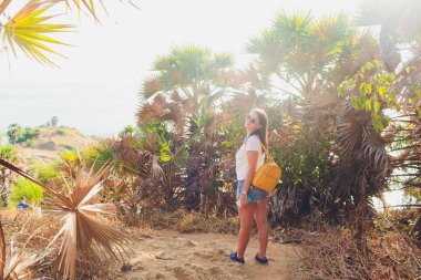Güzel bir kadın palmiye ağacının altında duruyor. Güneş parlak parlar. Kız mutlu.