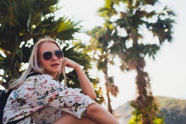 Tatil konsepti. Yaz keyfi. Gözlük Genç güzel kadın okyanus suyu üzerinde bir palmiye ağacında oturur.