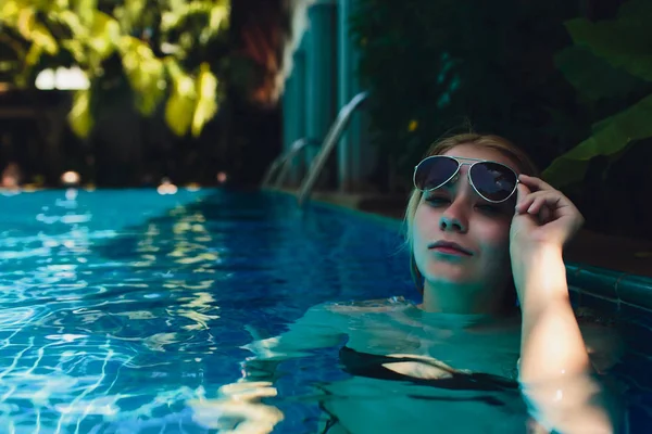 Gyönyörű nő relaxáló a medence víz. Lány az egészséges cserzett bőr, gyönyörű arc, és nedves Hair élvezi nyári nap a forró nyári napon a Pool Edge a Luxury Resort. — Stock Fotó