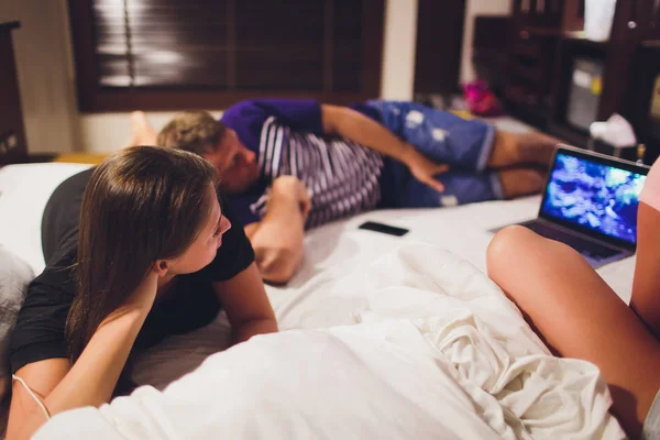 Couple watching tv in a laptop lying on a couch at home.