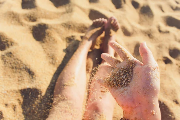 開いた手を通して走る砂の詳細。画像の隅には、砂で遊んでいる少女の髪の毛が見えます。. — ストック写真