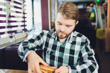 Taze lezzetli hamburger yeme ve kameraya arayan genç adam.