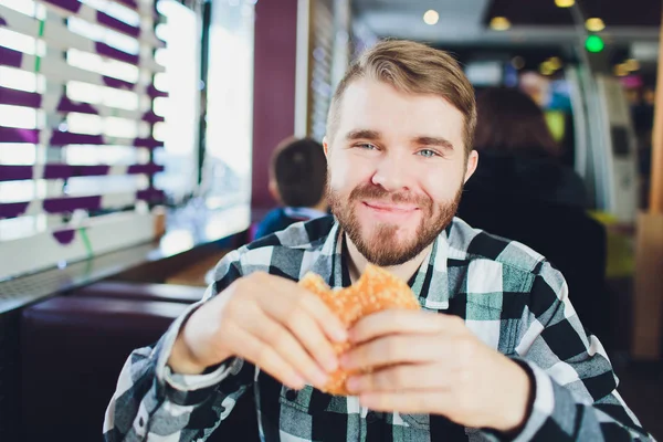 若い男の新鮮なおいしいハンバーガーをかむとカメラ目線. — ストック写真