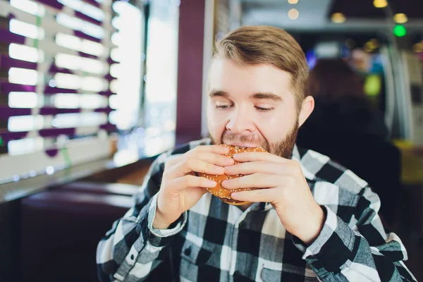 Jonge man bijten van verse, smakelijke hamburger en camera te kijken. — Stockfoto