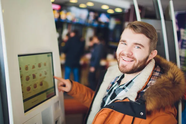 A man orders food in the touch screen terminal with electronic menu in fast food restaurant.