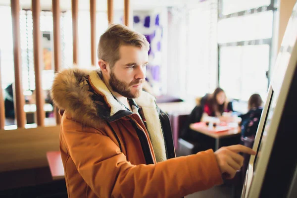 Un hombre pide comida en el terminal de pantalla táctil con menú electrónico en el restaurante de comida rápida . — Foto de Stock
