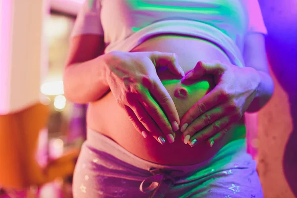 Mujer embarazada sosteniendo sus manos en forma de corazón en su protuberancia bebé. Embarazada Vientre con dedos Símbolo del corazón. Concepto de maternidad. Ducha bebé. — Foto de Stock