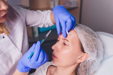 Doktor Kozmetolog, bir güzellik salonunda güzel, Genç bir kadının yüz derisi üzerinde kırışıklıkları sıkma ve yumuşatma için yüz enjeksiyonları prosedürü yapar. Kozmetoloji Cilt Bakımı.