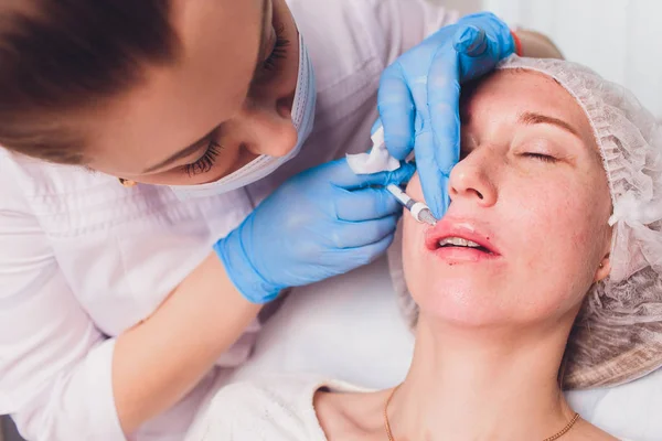 El médico cosmetólogo hace el procedimiento de aumento de labios de una mujer hermosa en un salón de belleza.. — Foto de Stock