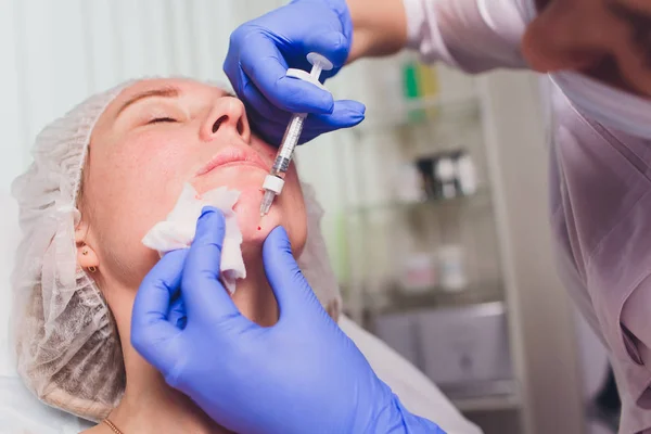 El médico cosmetólogo realiza un procedimiento de inyecciones faciales para apretar y alisar las arrugas en la piel de la cara de una hermosa mujer joven en un salón de belleza. Cosmetología cuidado de la piel . — Foto de Stock