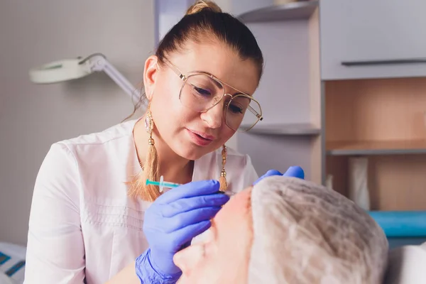 Il medico cosmetologo fa la procedura di iniezioni facciali per stringere e levigare le rughe sulla pelle del viso di una bella, giovane donna in un salone di bellezza. Cosmetologia cura della pelle . — Foto Stock