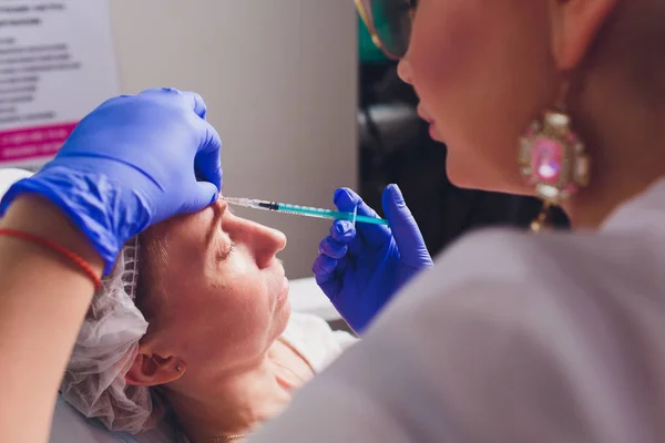 Il medico cosmetologo fa la procedura di iniezioni facciali per stringere e levigare le rughe sulla pelle del viso di una bella, giovane donna in un salone di bellezza. Cosmetologia cura della pelle . — Foto Stock