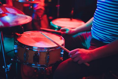 Adam siyah arka plana yakın sopalarla müzik aleti çalıyor. Davul çalan bir müzik konsepti, sahnede güzel bir ışıklandırma..