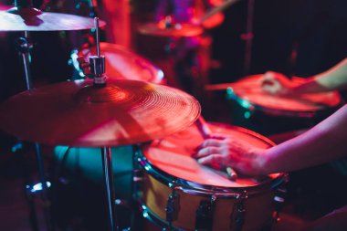 Adam siyah arka plana yakın sopalarla müzik aleti çalıyor. Davul çalan bir müzik konsepti, sahnede güzel bir ışıklandırma..