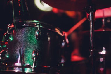 Adam siyah arka plana yakın sopalarla müzik aleti çalıyor. Davul çalan bir müzik konsepti, sahnede güzel bir ışıklandırma..