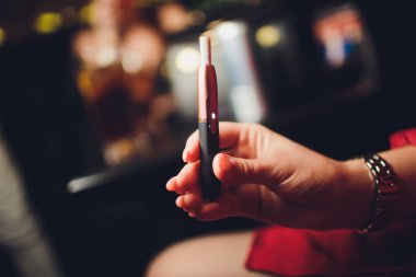 Elektronik Sigara, teknoloji sigara. Tütün sistemi Iqos. Restoran bulanık arka planda kadın el. Kırmızı kasa.
