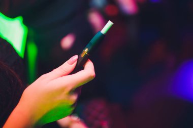 Elektronik Sigara, teknoloji sigara. Tütün sistemi Iqos. Restoran bulanık arka planda kadın el. siyah kasa.