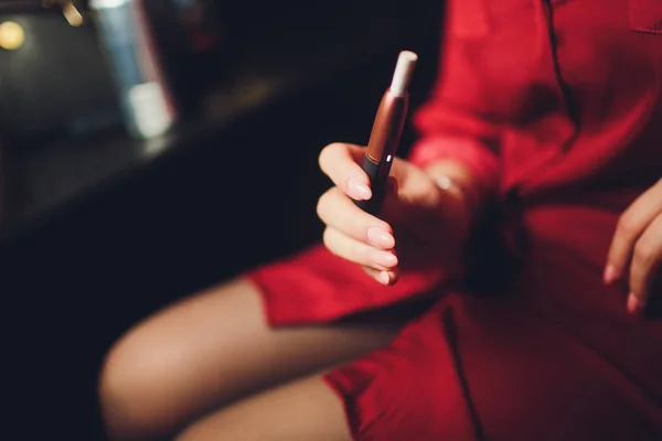 Cigarros electrónicos, cigarros tecnológicos. Sistema de tabaco IQOS. Mão feminina no fundo turvo do restaurante. caso vermelho . — Fotografia de Stock