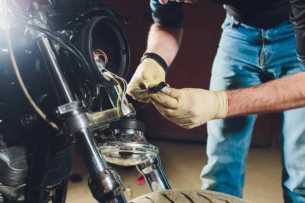 Hombre arreglando bicicleta. Joven confiado reparando motocicletas cerca de su garaje. lámpara de repuesto en el faro — Foto de Stock