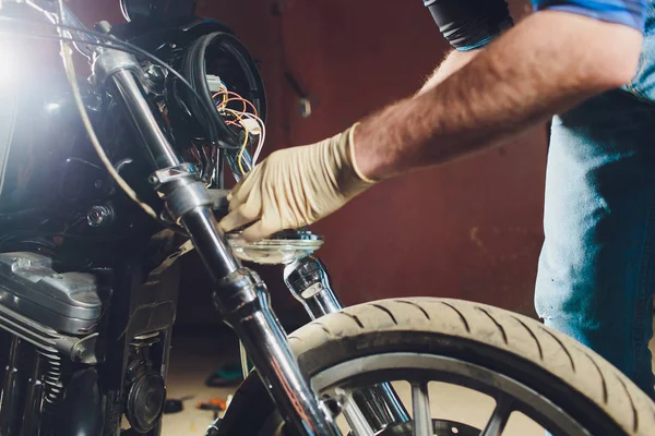 Hombre arreglando bicicleta. Joven confiado reparando motocicletas cerca de su garaje. lámpara de repuesto en el faro — Foto de Stock