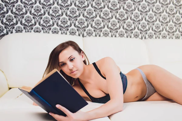 Vrouw liggen op een sofa tijdens het lezen van een boek in een woonkamer. — Stockfoto