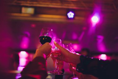 Genç arkadaşlar ellerinde şampanya kadehleriyle dans ediyorlar. Arka plan olarak ışıklandırma cihazlarına karşı. Genç insanlar dans ediyor..