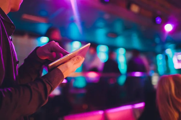 Event tuner controlling sound from tablet on the background of karaoke bar.