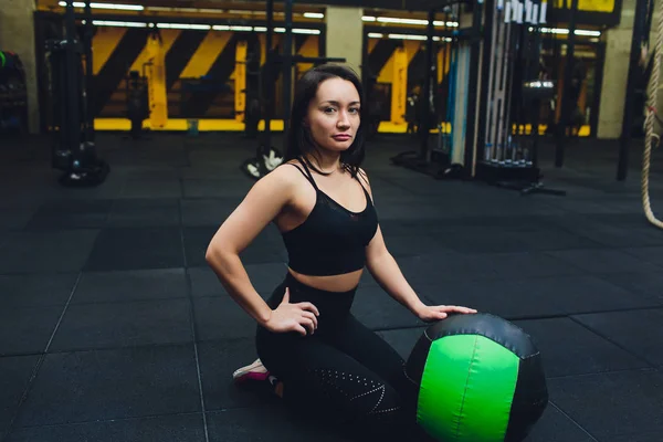 Muscular woman doing intense core workout in gym. Strong female doing core exercise on fitness mat with medicine ball in health club.