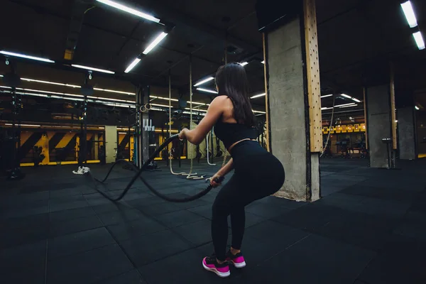 Mujer entrenando con cuerdas de batalla en el gimnasio, haciendo un intenso entrenamiento duro . —  Fotos de Stock