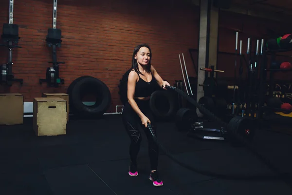 Woman training with battle ropes in gym, doing intense hard training.