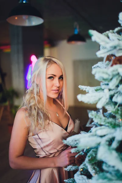 Módní fotka nádherné ženy se světlými vlasy v luxusních šatech představujících pokoj s vánočním stromku a dekoracemi. — Stock fotografie