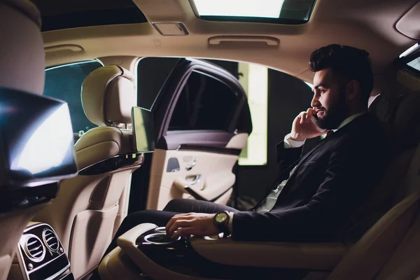 Retrato de hombre de negocios barbudo guapo hablando por teléfono sentado en el asiento trasero del coche . —  Fotos de Stock