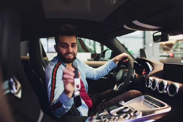 Retrato joven feliz hombre mostrando las llaves sentado en nuevo coche . — Foto de Stock