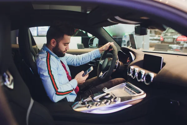 Siempre en contacto. Vista trasera superior del joven en ropa formal usando su teléfono inteligente mientras está sentado en el coche . — Foto de Stock