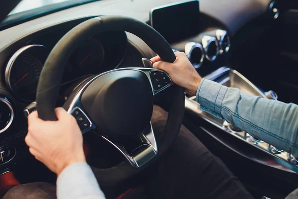 Empresario que conduce un coche moderno de lujo en la ciudad. Primer plano mans mano en el volante del coche . — Foto de Stock