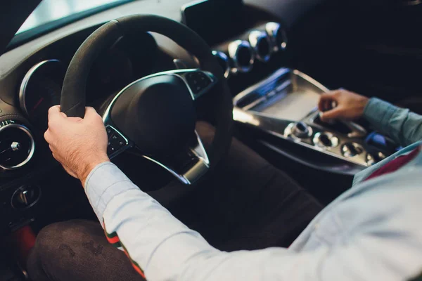 Empresario que conduce un coche moderno de lujo en la ciudad. Primer plano mans mano en el volante del coche . — Foto de Stock