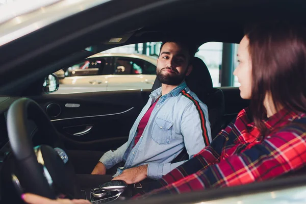 Visitando concesionario de coches. Hermosa pareja está hablando y sonriendo mientras está sentado en su nuevo coche. Mujer conduciendo su coche nuevo en el distribuidor — Foto de Stock