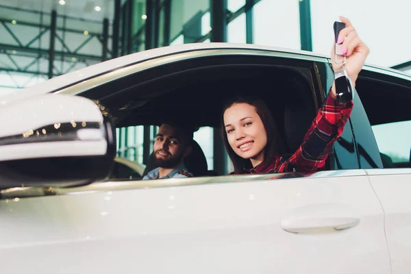 Foto de una joven sonriente mujer de raza mixta sentada dentro de su nuevo coche y sosteniendo la llave. Concepto de alquiler de coches . — Foto de Stock