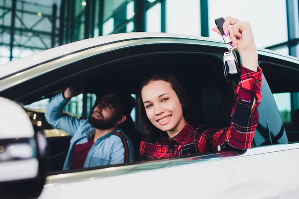 Foto de una joven sonriente mujer de raza mixta sentada dentro de su nuevo coche y sosteniendo la llave. Concepto de alquiler de coches . — Foto de Stock