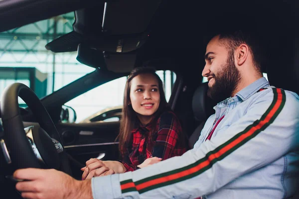 Visitando concesionario de coches. Hermosa pareja está hablando y sonriendo mientras está sentado en su nuevo coche. hombre conduciendo su coche nuevo en el distribuidor — Foto de Stock