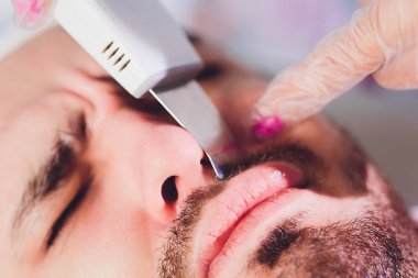 Ultrasonik yüz temizliği, Genç adam. Kozmetolog işi yakın. Cilt Bakım Teknolojileri Araştırma. Makro. burun prosedürü