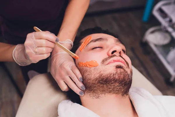Hair removal. Mans face sugaring epilations beard trimming, yellow color, in cosmetology on the couch.
