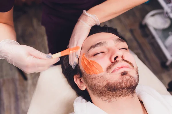 Depilazione. Gli uomini affrontano epilazioni zuccherine taglio della barba, colore giallo, in cosmetologia sul divano . — Foto Stock