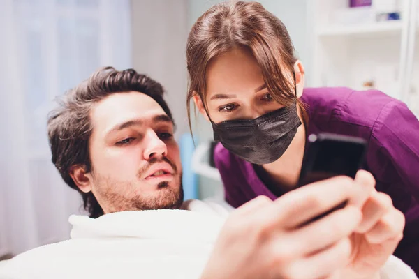 Hombre y médico antes de la cirugía plástica. Médico sosteniendo la tableta y hablando con su paciente . — Foto de Stock