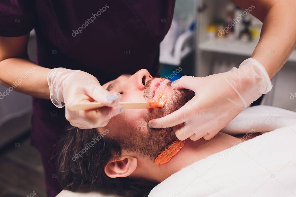 Hair removal. Mans face sugaring epilations beard trimming, yellow color, in cosmetology on the couch.